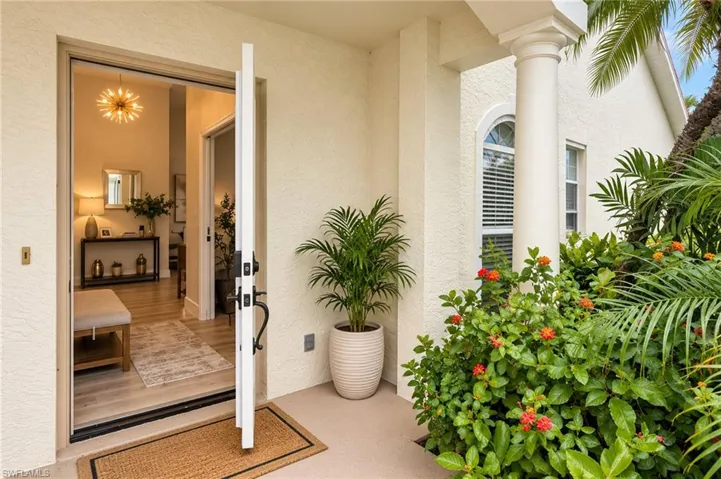 Welcoming entry with a substantial white door, decorative lighting, wood-finish flooring, and lush landscaping