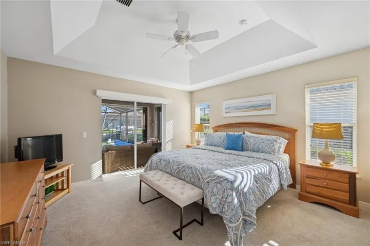 Carpeted bedroom with ceiling fan, access to exterior, baseboards, and a raised ceiling