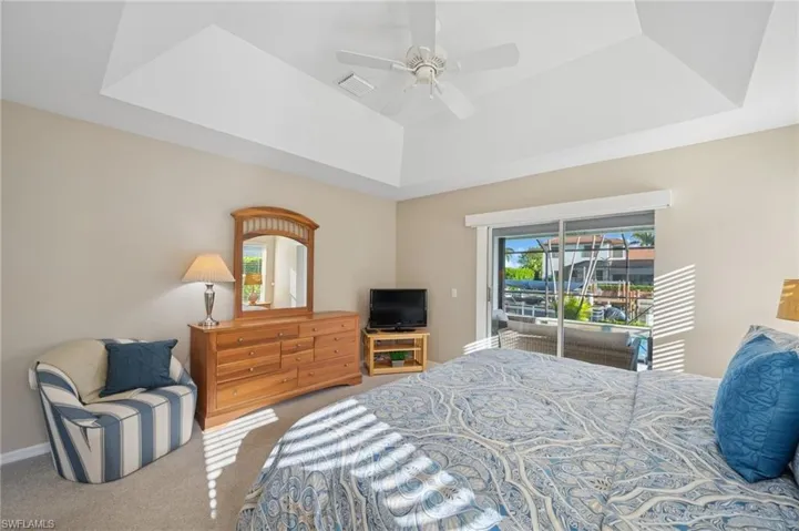 Bedroom with ceiling fan, carpet, visible vents, access to exterior, and a raised ceiling