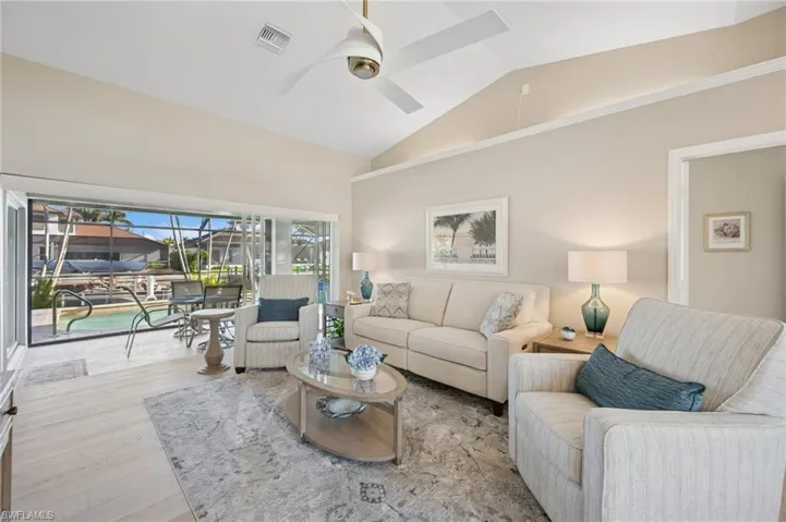 Living area with high vaulted ceiling, visible vents, wood finished floors, and ceiling fan