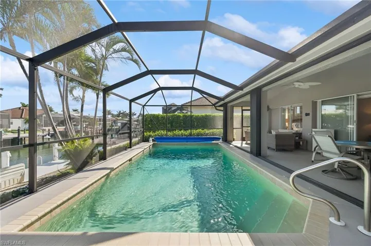 Outdoor pool with a patio area, ceiling fan, and glass enclosure