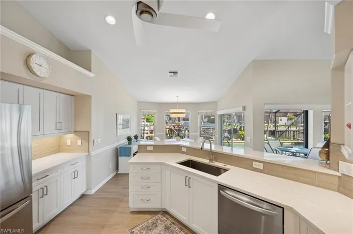 Kitchen with a sink, appliances with stainless steel finishes, vaulted ceiling, backsplash, and light stone counters