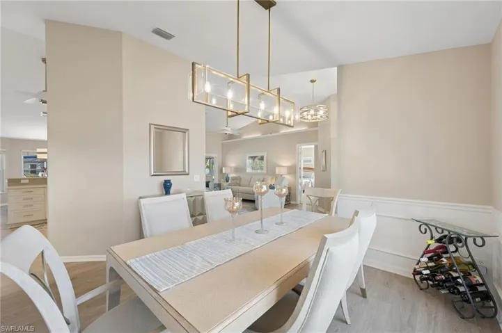 Dining space featuring a towering ceiling, light wood-type flooring, an inviting chandelier, visible vents, and wainscoting