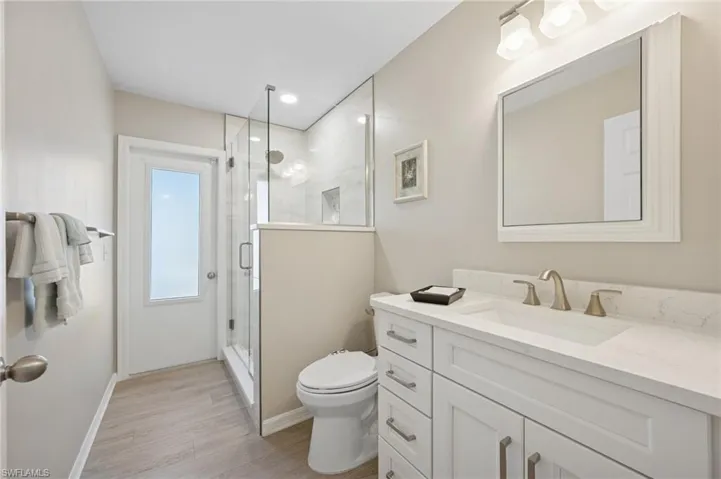 Bathroom with toilet, vanity, wood finished floors, and baseboards