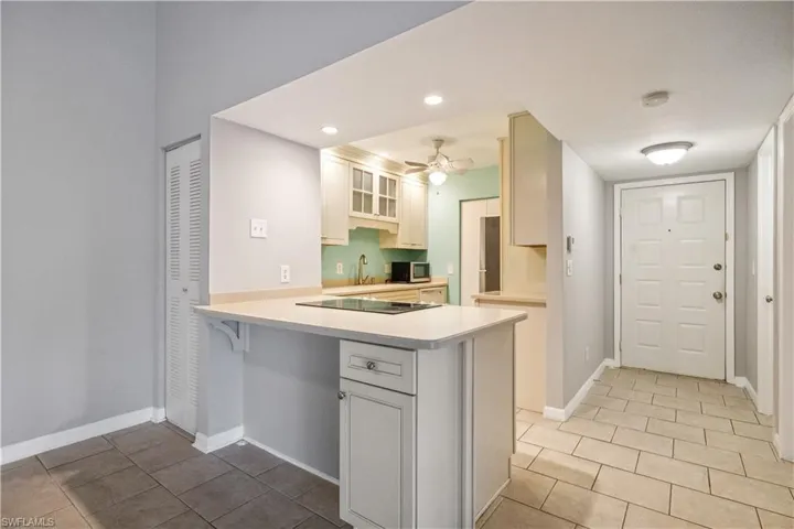Kitchen with stainless steel microwave, a peninsula, black electric stovetop, light countertops, and light tile patterned floors
