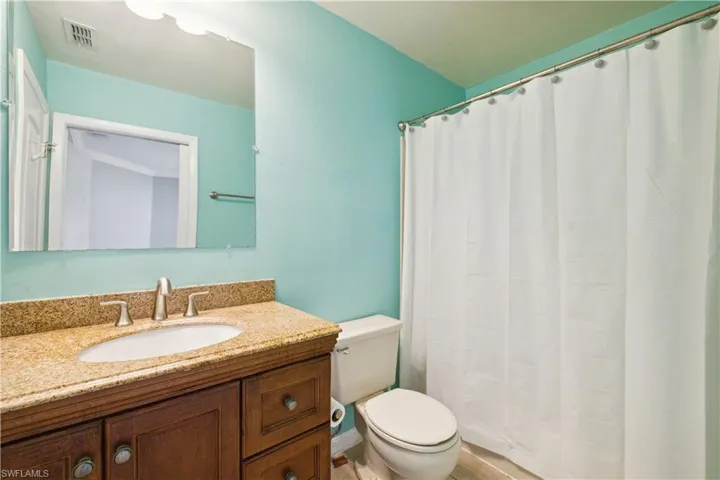 Full bath with toilet, a shower with curtain, vanity, and visible vents
