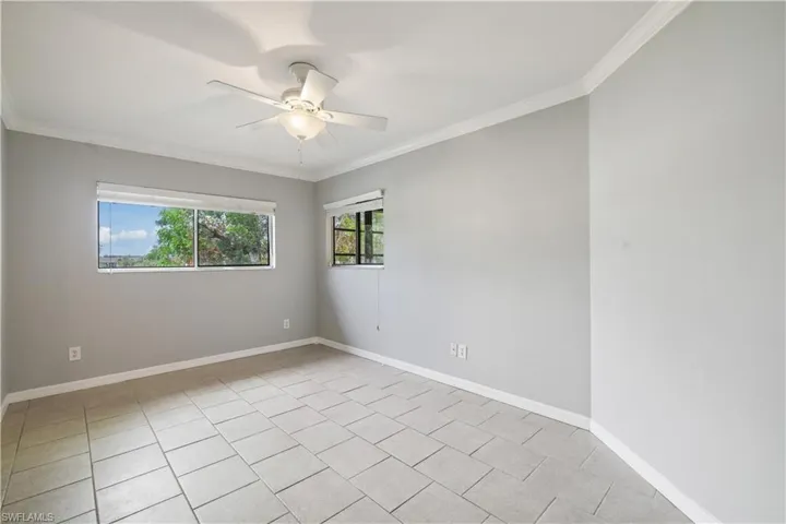 Spare room featuring crown molding, light tile patterned floors, baseboards, and ceiling fan