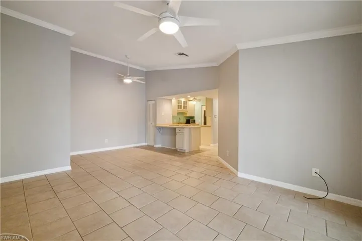 Unfurnished living room with lofted ceiling, visible vents, ceiling fan, crown molding, and light tile patterned floors