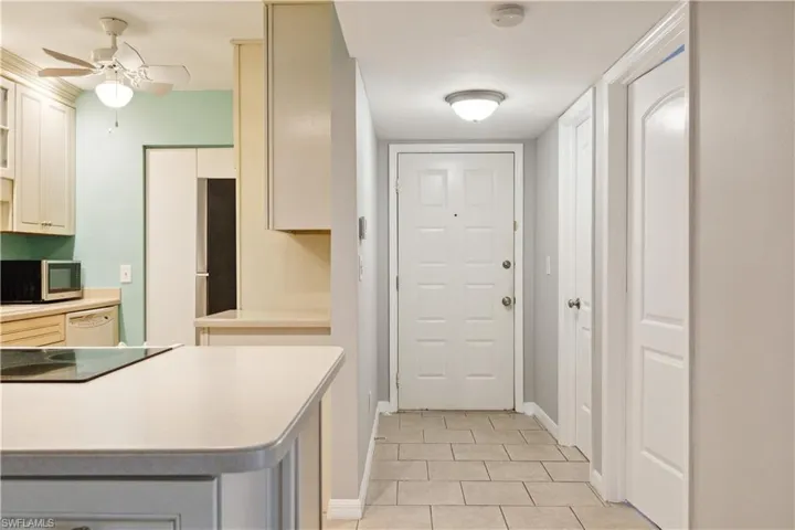 Kitchen featuring stainless steel microwave, light tile patterned flooring, ceiling fan, light countertops, and white dishwasher
