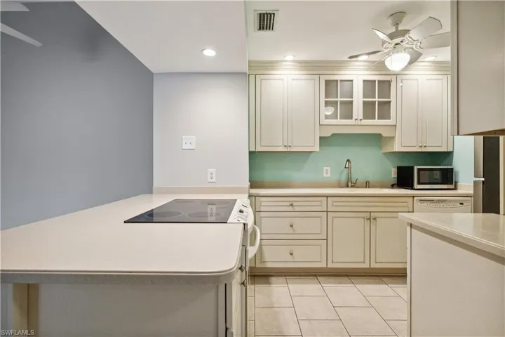 Kitchen with stainless steel microwave, a peninsula, a sink, ceiling fan, and light countertops