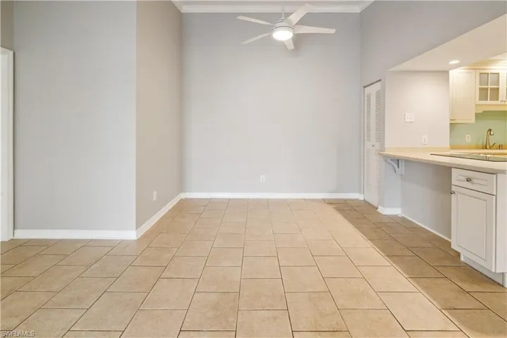 Kitchen with a ceiling fan, a sink, white cabinetry, light countertops, and ornamental molding
