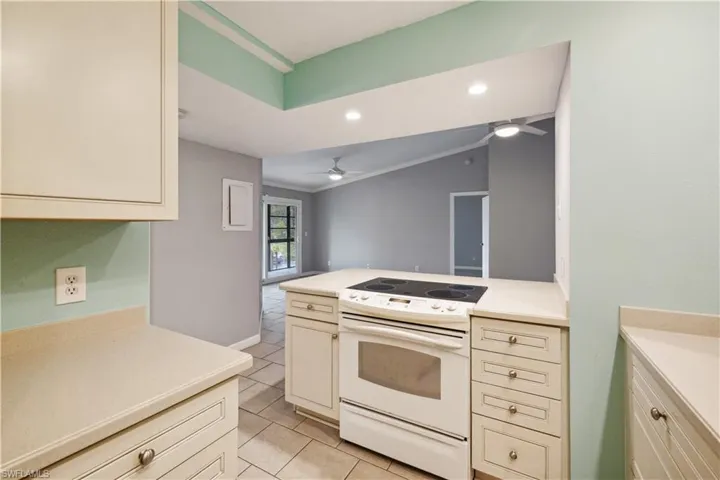 Kitchen with a ceiling fan, light tile patterned floors, white range with electric stovetop, cream cabinetry, and light countertops