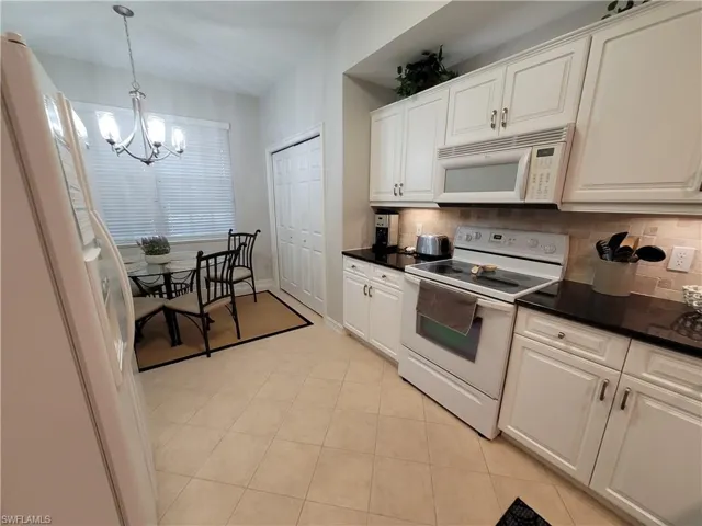 Kitchen with decorative light fixtures, white appliances, backsplash, and light tile flooring