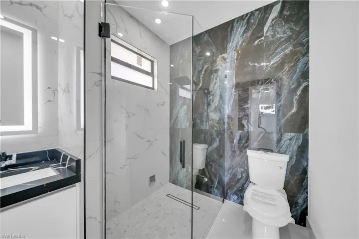 Full bath with stone wall, vanity, a marble finish shower, marble tiled floors, and tile walls