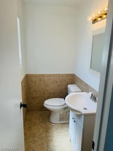 Bathroom with tile flooring, vanity, toilet, and tile walls