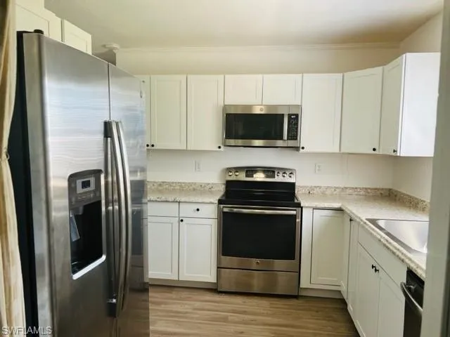 Kitchen with light wood-luxury Vinyl flooring,appliances with stainless steel finishes, white cabinets, light stone counters, and sink