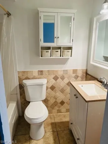 Full bathroom featuring tile floors, oversized vanity, toilet, and tile walls
