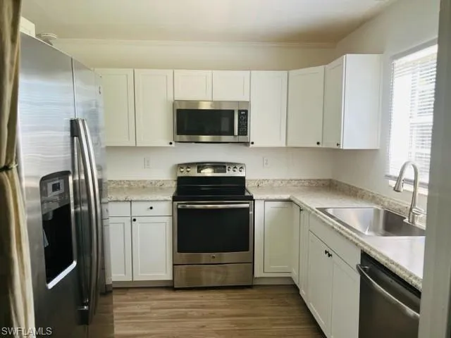 Kitchen featuring stainless steel appliances, sink, hardwood / wood-style floors, and white cabinets