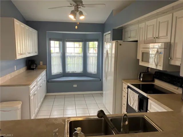 Kitchen featuring ceiling fan, sink, vaulted ceiling, white appliances, and light tile patterned floors