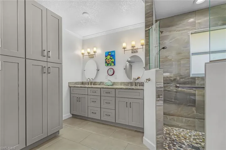 Bathroom with double vanity, a textured ceiling, crown molding, a shower stall, and light tile patterned floors