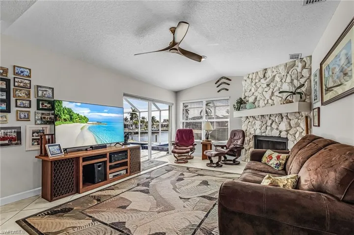 Living room with a stone fireplace, lofted ceiling, tile patterned flooring, a ceiling fan, and a textured ceiling