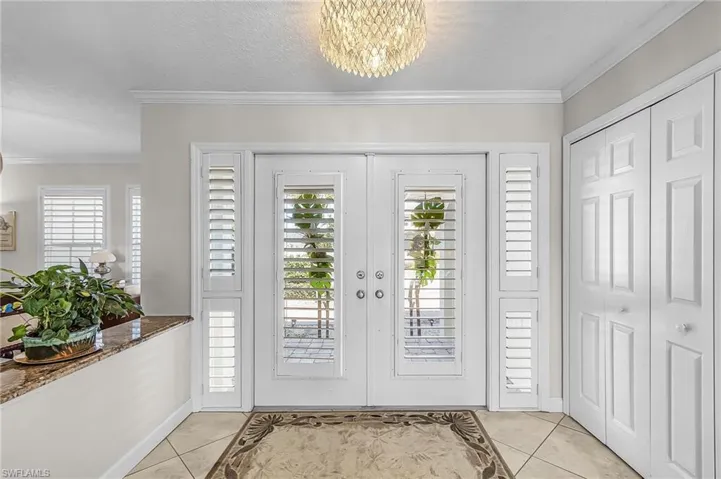 Entryway with french doors, a chandelier, crown molding, light tile patterned floors, and a textured ceiling