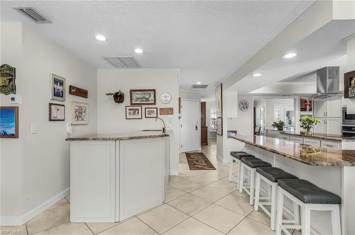 Kitchen featuring a peninsula, dark stone countertops, white cabinets, a textured ceiling, and a kitchen bar