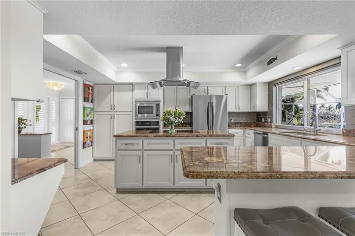Kitchen featuring island exhaust hood, dark stone countertops, crown molding, recessed lighting, and a kitchen bar