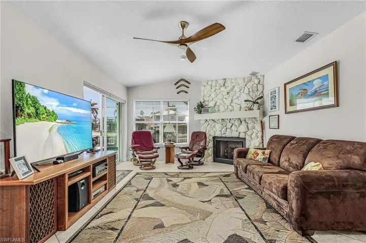 Living room featuring a stone fireplace, a ceiling fan, lofted ceiling, a textured ceiling, and tile patterned floors
