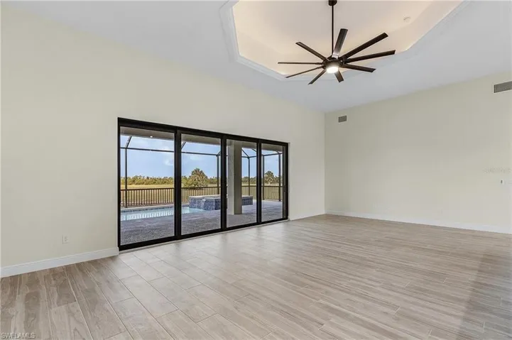 Empty room with a raised ceiling, light wood-type flooring, and ceiling fan