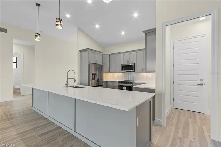 Kitchen featuring tasteful backsplash, pendant lighting, sink, a center island with sink, and appliances with stainless steel finishes
