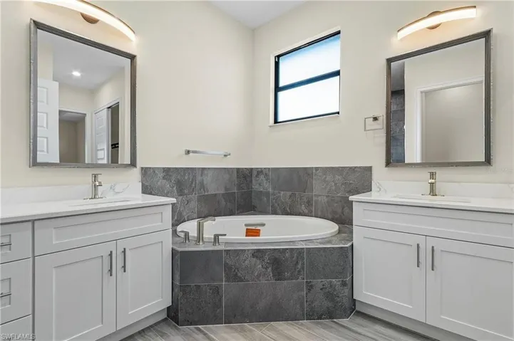 Bathroom featuring a relaxing tiled tub, dual vanity, and hardwood / wood-style floors