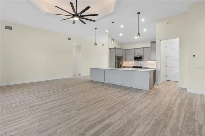 Kitchen with an island with sink, gray cabinets, ceiling fan, hanging light fixtures, and appliances with stainless steel finishes