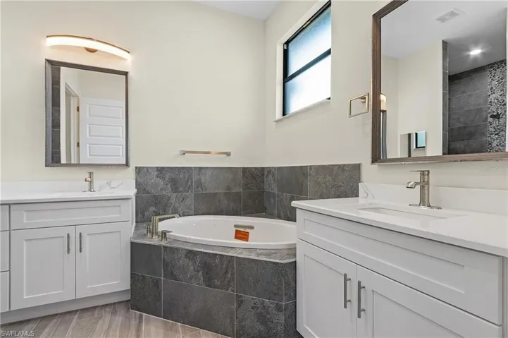 Bathroom featuring a relaxing tiled tub, tile patterned flooring, and double sink vanity