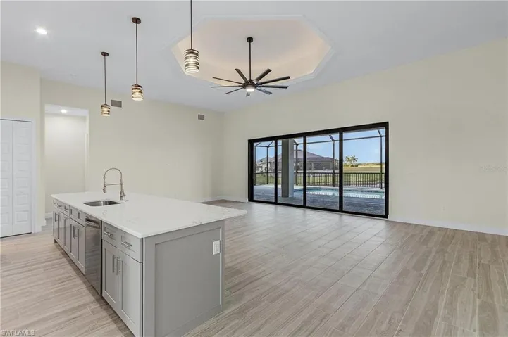 Kitchen featuring gray cabinets, decorative light fixtures, ceiling fan, an island with sink, and sink