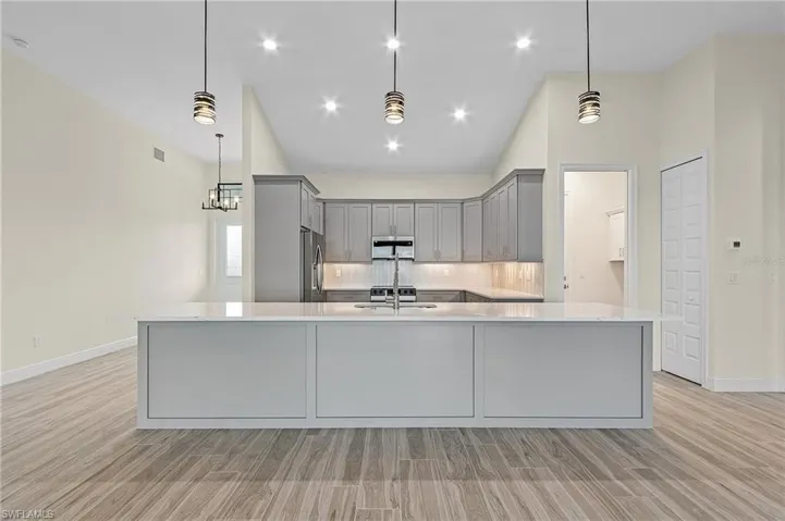 Kitchen featuring tasteful backsplash, gray cabinets, stainless steel appliances, light hardwood / wood-style floors, and pendant lighting