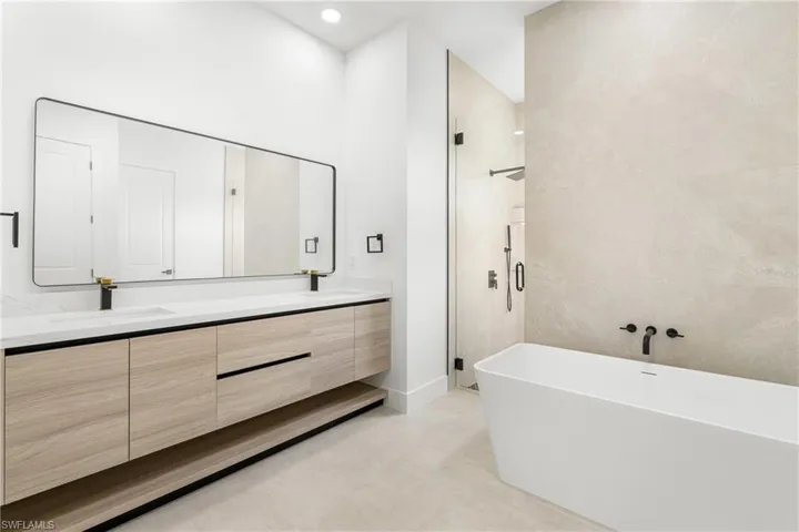 Contemporary bathroom featuring a freestanding tub, glass-enclosed shower, dual vanity with light wood-finish cabinetry, white countertops, and integrated sinks