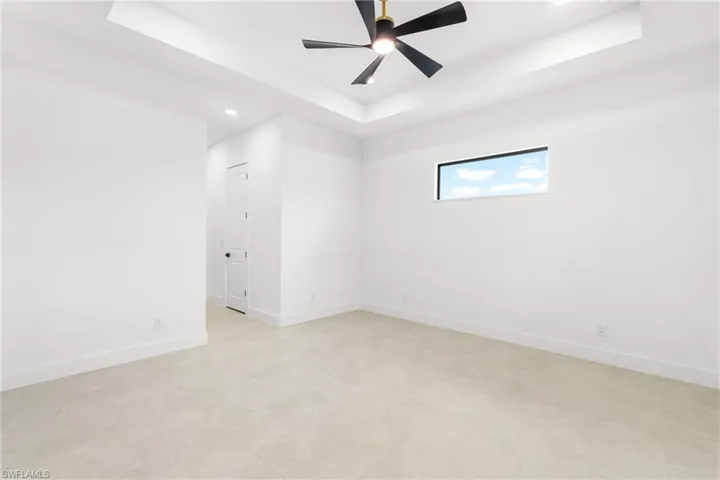 Spacious room featuring a tray ceiling with a modern ceiling fan, a horizontal window, light-colored tile flooring, and white baseboards