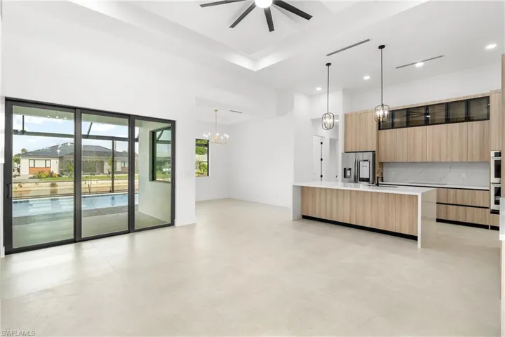 Modern open-concept living space featuring expansive sliding glass doors, a kitchen island with a waterfall countertop, contemporary wood-finish cabinetry, integrated stainless steel appliances, and sleek pendant lighting