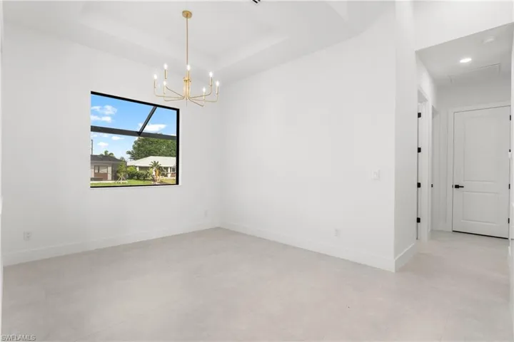 Spacious room featuring a contemporary gold-finish chandelier, tray ceiling, and light-toned tile flooring