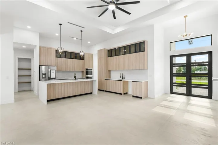 Modern kitchen featuring light wood-finish cabinetry, integrated stainless steel appliances, and a waterfall island with a sink and pendant lighting