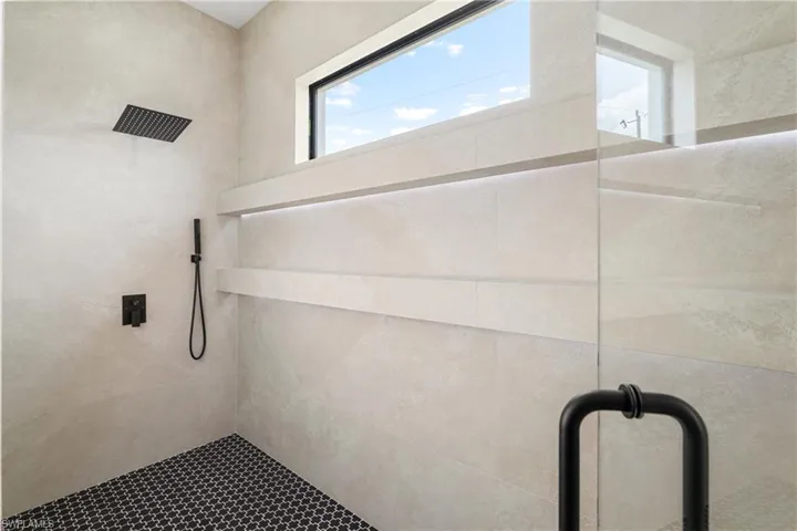 Shower stall featuring black arabesque floor tiling, matte black fixtures, an overhead rain shower, built-in shelving with integrated lighting, and a clear glass enclosure