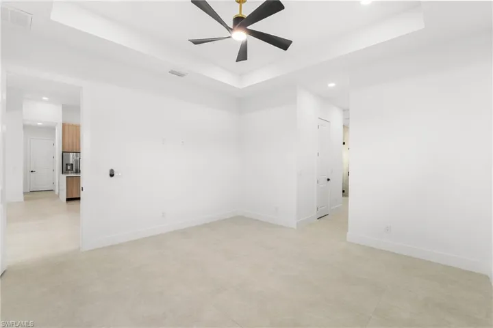 Spacious room featuring light-toned tile flooring, a tray ceiling, and a contemporary ceiling fan with a gold-tone base
