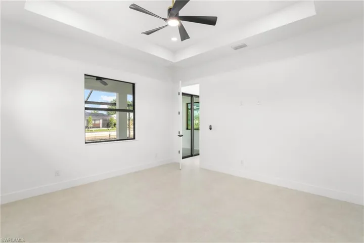 Spacious room featuring a tray ceiling with a ceiling fan, a large window with black framing, and neutral tone tile flooring