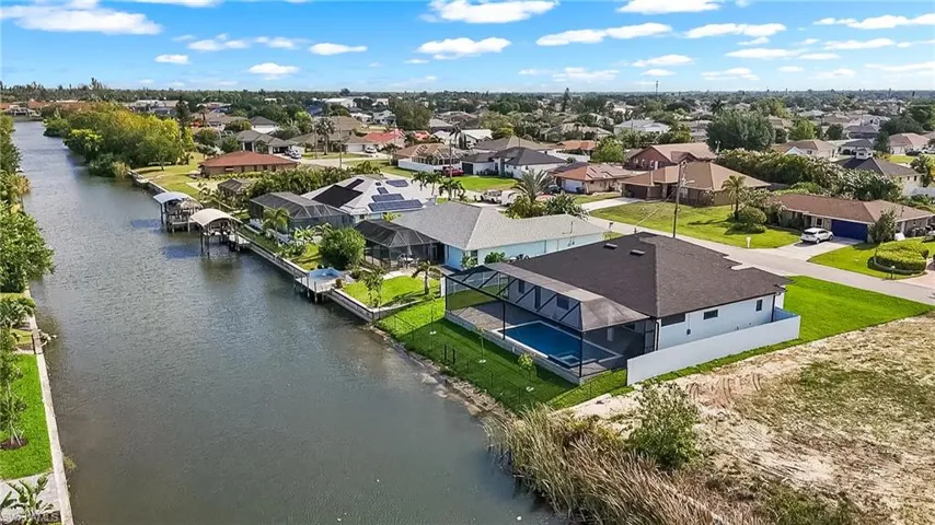 Canal-front property featuring a screened-in pool enclosure, private dock with boat lift, and lush green landscaping