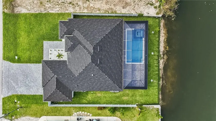 New construction home featuring a dark shingle roof, lush green lawn, and a paved driveway