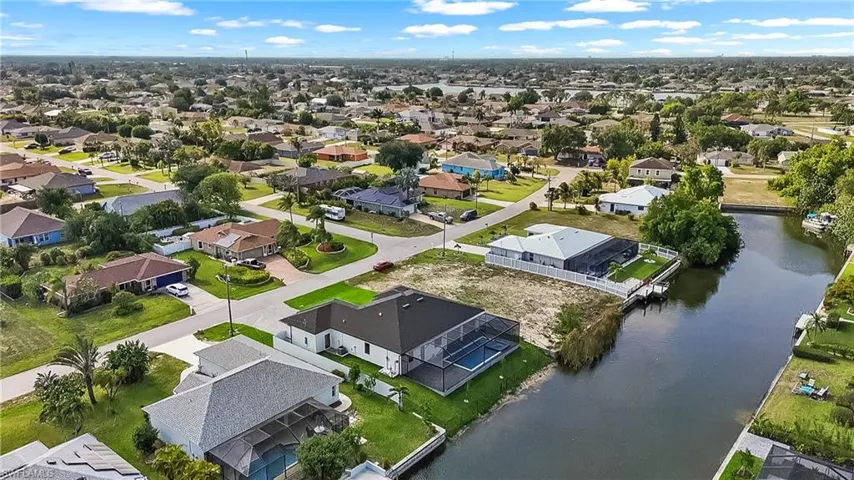 Waterfront property featuring a private boat dock, screened pool enclosure, paved driveway, and mature landscaping