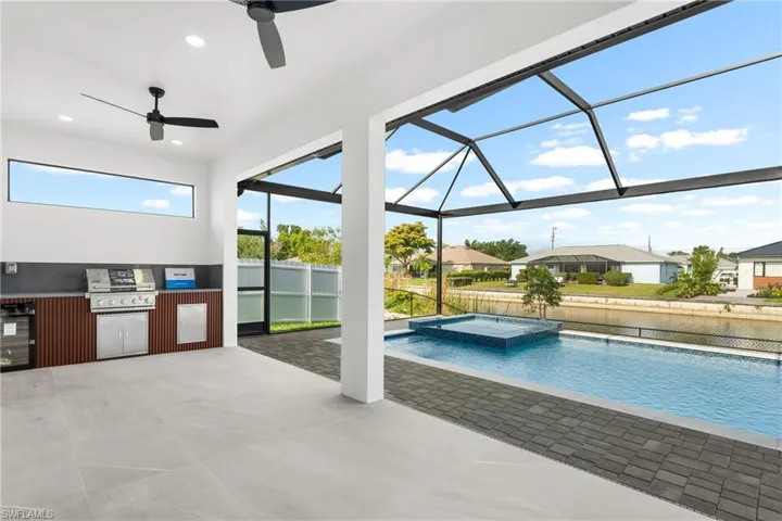 Expansive screened lanai featuring an outdoor kitchen with stainless steel appliances and wood-finish cabinetry