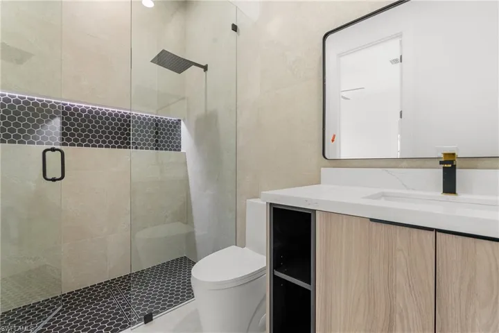 Glass-enclosed shower with black hexagonal tile flooring and an illuminated niche