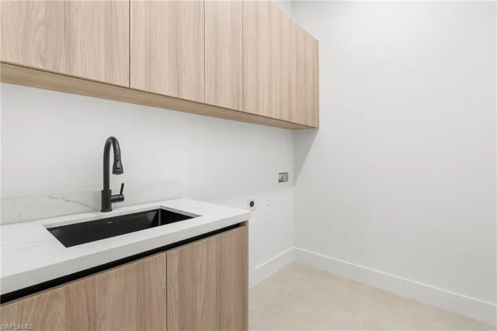 Utility area featuring wood-finish cabinetry, a white countertop with integrated sink, and a matte black faucet